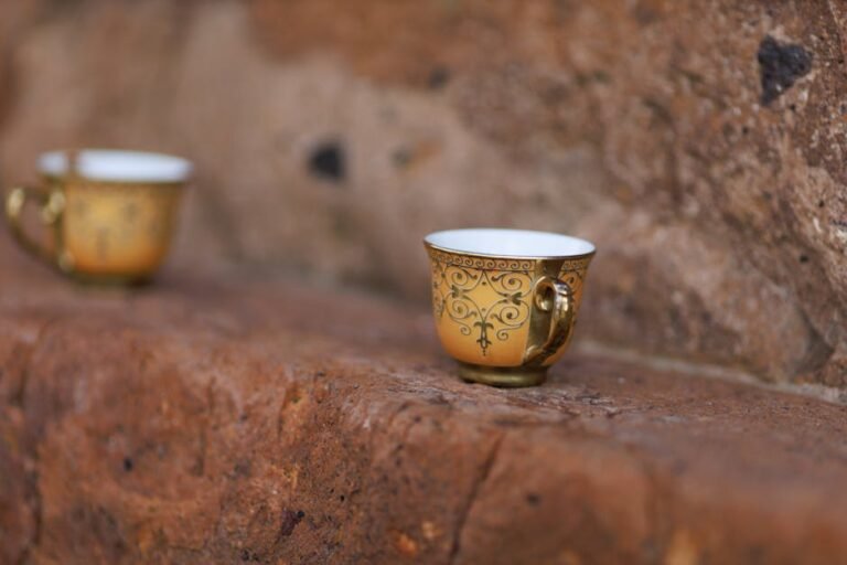 A close-up of a decorative golden teacup resting on a rustic stone surface outdoors.