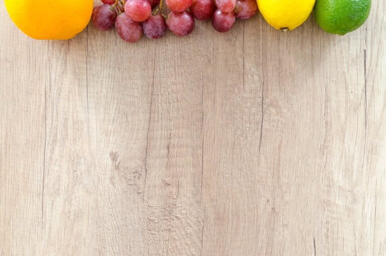 Fresh oranges, grapes, lemon, and lime arranged on a wooden chopping board, offering vibrant colors.