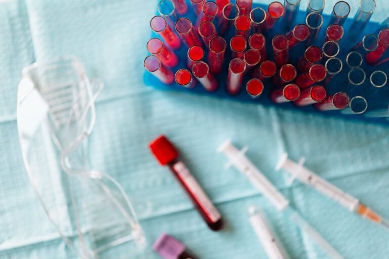 Overhead shot of blood samples, syringes, and safety goggles in a medical lab setting.