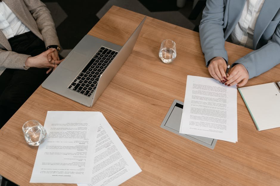 Two professionals hold a meeting with documents and a laptop on a wooden desk.