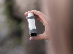 A person holding a gray asthma inhaler outdoors. Health and medical concept.
