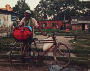 A man stands beside his bicycle on a street in Sylhet, Bangladesh, during dusk.