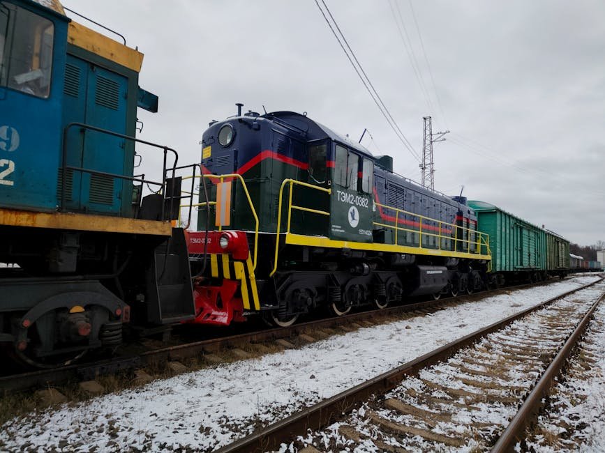 A colorful freight train on snowy tracks during winter on a cloudy day.