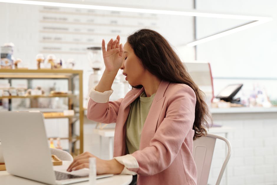 Young woman feeling unwell while working on her laptop indoors, looking fatigued.