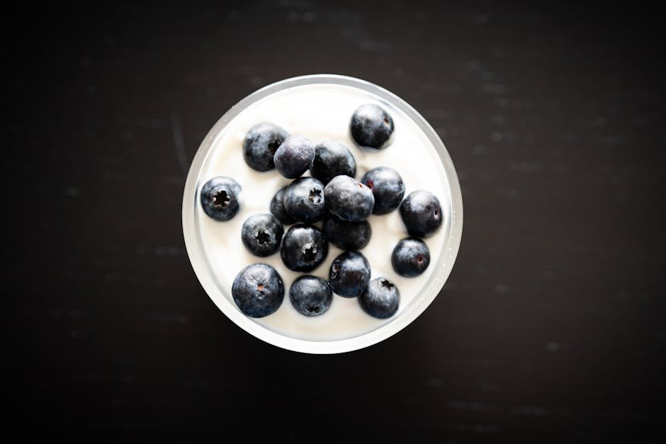 Top view of creamy yogurt with fresh blueberries in a glass bowl on a dark background.