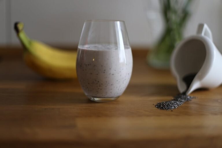Glass of chia seed smoothie with banana and spilled seeds on wooden table.