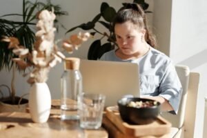 Young woman with Down syndrome using a laptop at a cozy home setting, enjoying leisure time.
