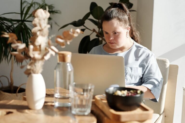 Young woman with Down syndrome using a laptop at a cozy home setting, enjoying leisure time.