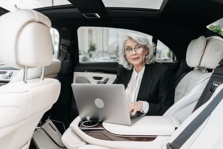 Senior businesswoman using laptop inside a luxury car with modern interior.