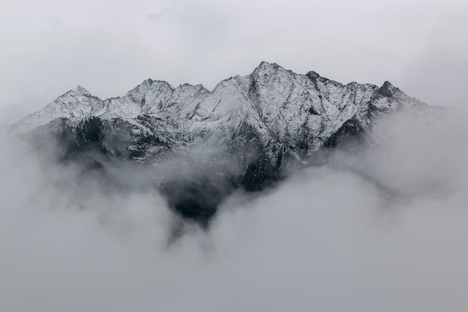 A breathtaking view of snow-covered mountain peaks surrounded by dense fog, creating a mystical landscape.