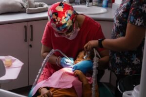 A child receives dental care from a dentist with an assistant in a brightly decorated clinic.