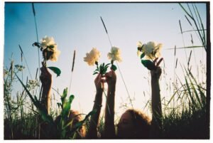 Two women raise white flowers in a sunny field, capturing summer joy and freedom.