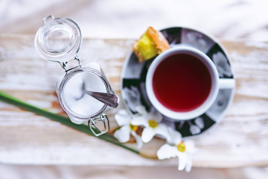 Overhead view of a tea set with sugar jar, flower decor, and pastry on rustic background.